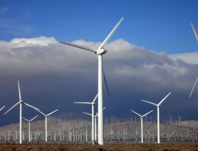 White wind turbine towers generating green energy under a blue sky.