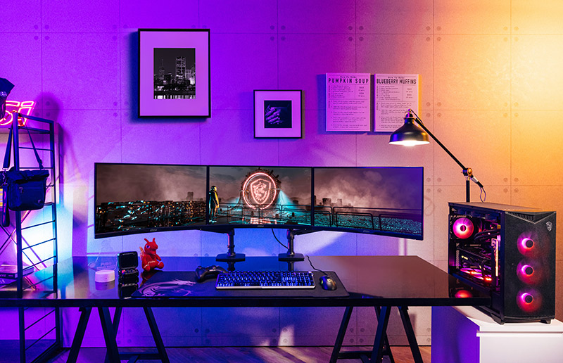 A high-end gaming PC setup featuring a triple monitor display and vibrant RGB lighting in a modern room.