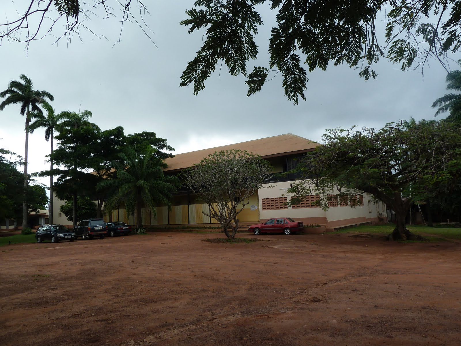 Exterior view of a building with parked cars and palm trees in Kumasi, Ghana.
