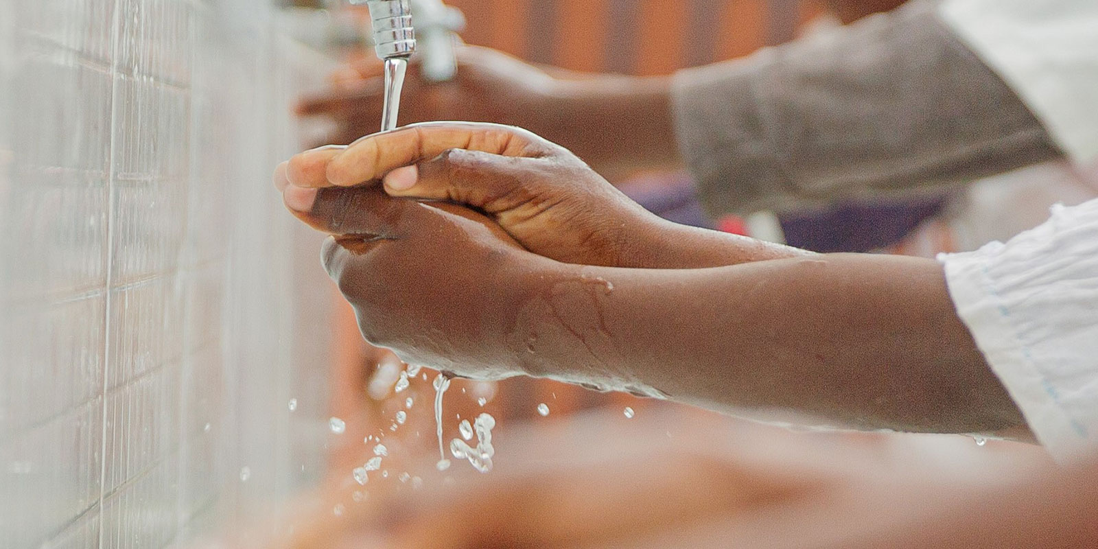 A person washing their hands under running water at a sink.