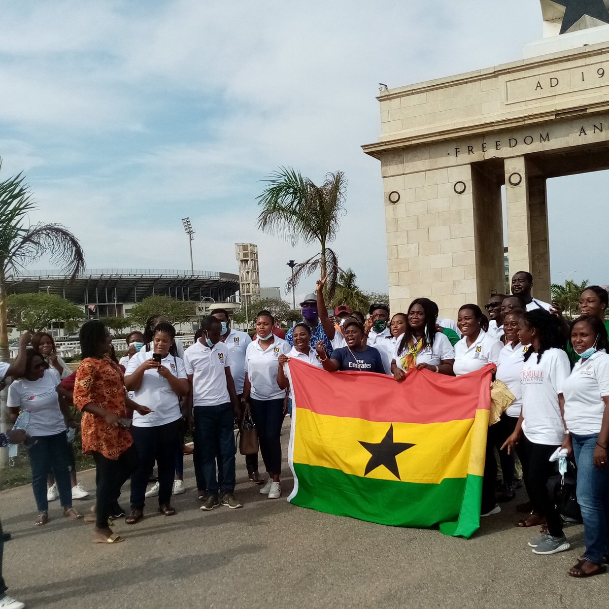 A group of people gathering with the national flag of Ghana near the Black Star Square and Independence Arch in Accra.