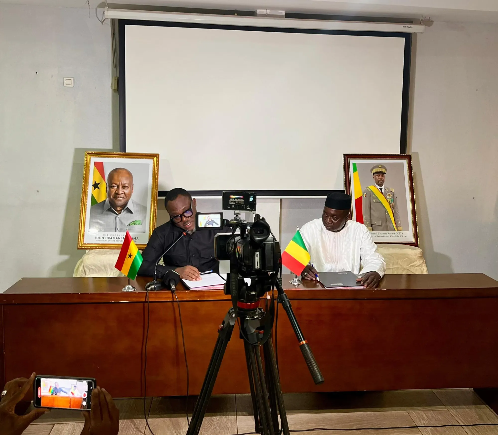 A press conference or official meeting setup featuring representatives with the flags of Ghana and Mali, captured in Bamako, Mali.