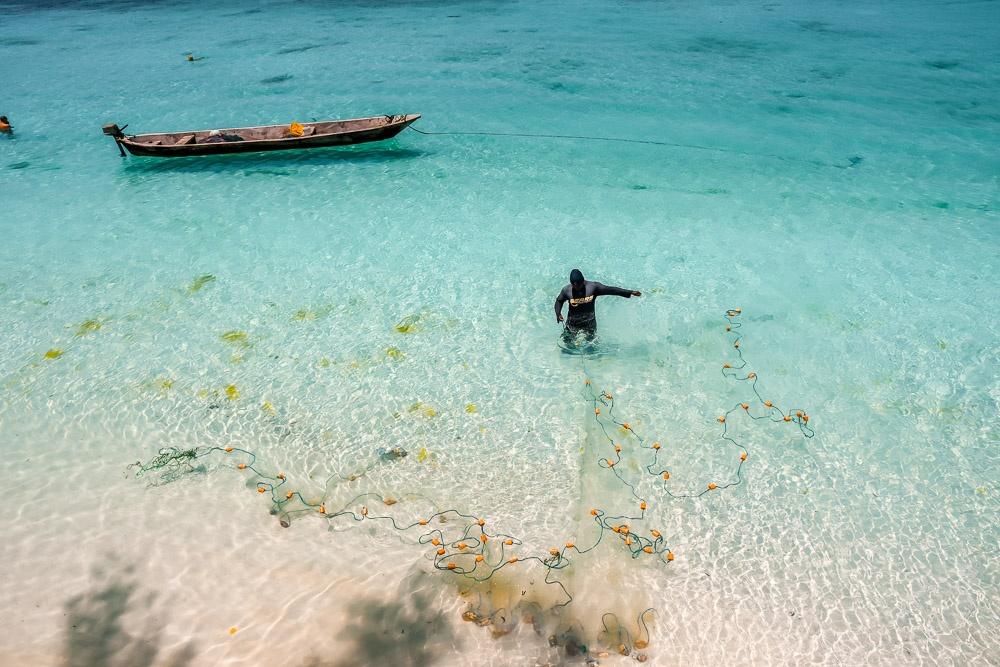 A person fishing with a net in the clear shallow waters of Zanzibar, Tanzania.