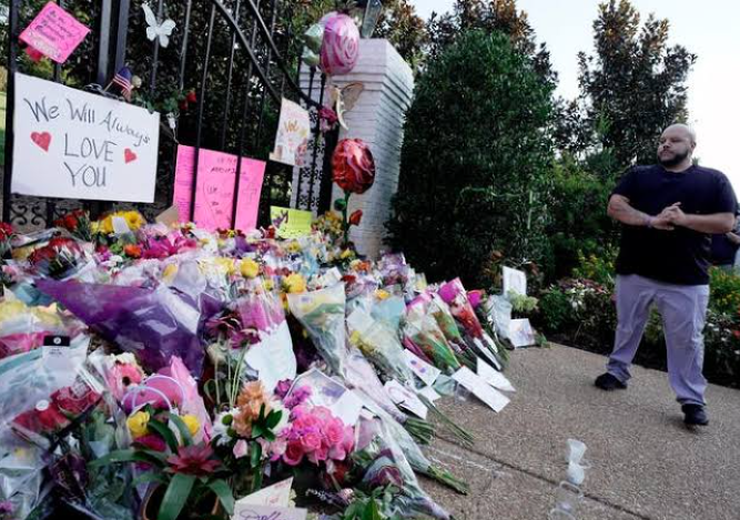 A man standing near a massive floral tribute and memorial outside the home of the late country music star Loretta Lynn in Hurricane Mills, Tennessee.