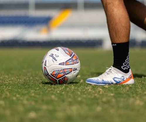 Soccer player on a green turf field inside a stadium next to a patterned soccer ball.
