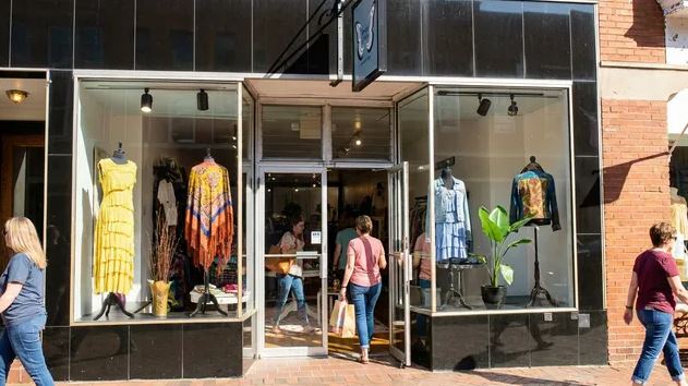 Shoppers walking past a modern fashion retail storefront window.