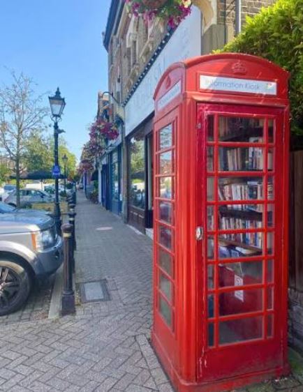 Red telephone box on a London sidewalk with modern glass architecture behind it.
