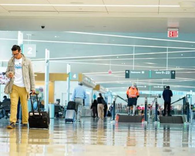 Travelers walking through a busy airport terminal departure gate area.