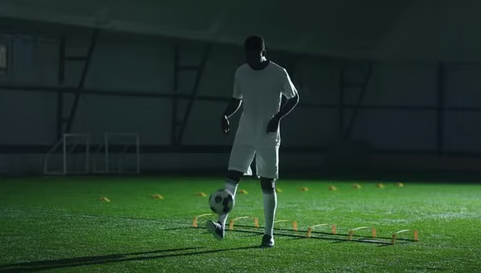 A soccer player practicing footwork and juggling a ball during training on an indoor turf pitch.
