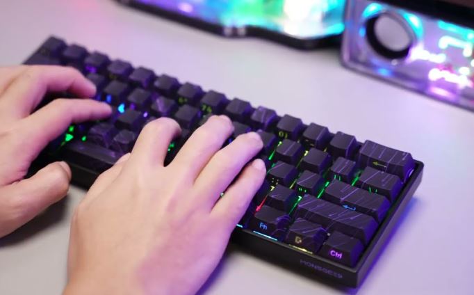 Close-up of hands typing on a laptop keyboard next to a desk lamp.
