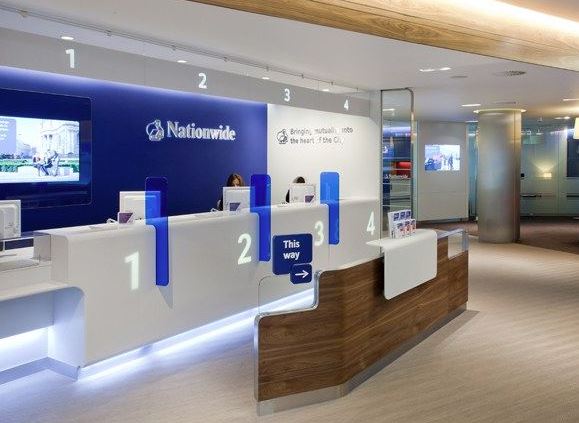 Modern retail bank branch interior featuring customer service teller windows and digital display screens.