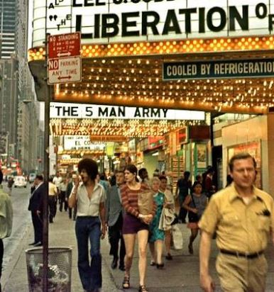 People walking through a brightly lit cinema foyer near digital movie posters.